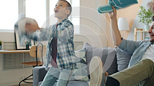 Dad and son watching football on TV celebrating victory throwing ball having fun at home