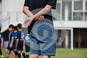 Dad standing and watching his son playing football in a school tournament on a sideline with a sunny day.