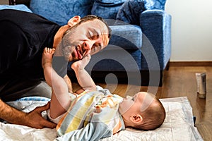Dad struggling with his baby daughter to change dirty diapers putting faces of effort, concept of fatherhood