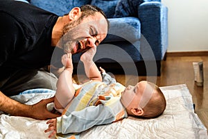 Dad struggling with his baby daughter to change dirty diapers putting faces of effort, concept of fatherhood