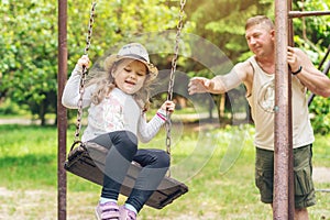 Dad swings his little happy daughter on a swing on a warm sunny day