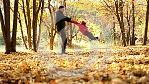 Dad swirles small daughter for the hands in an autumn park against a backdrop of trees and fallen yellow leaves