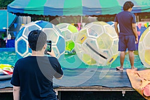 Dad take a photo by smartphone of his son having fun in giant bubble ball on water in pool