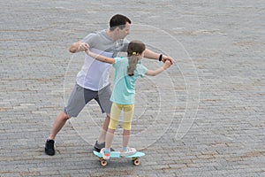 Dad teaches daughter to skateboard in a city park