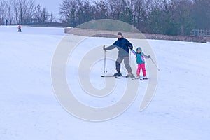 Dad teaches daughter to ski. A skier holds a little girl by the hand and helps to ski. An instructor teaches a child winter sports