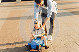 Dad teaches his little son to ride a children`s car in the park, keep balance, have fun with the family