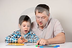 Dad teaches his son to read, names and write letters together. Parent prepares child for school.