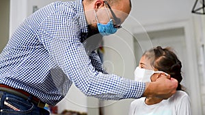 Dad tries on a medical mask for her little daughter. Stay home mom. Coronavirus or COVID-19. Dad teaches daughter to put on a medi