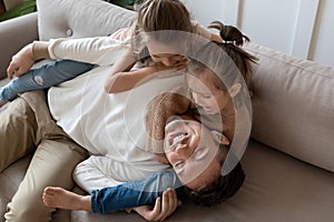 Dad and two cute daughter play together lying on couch