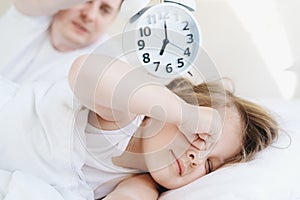 Dad wakes up little sleeping in bed girl,daughter. Big alarm clock. Early morning before kindergaten, school. White pillow,