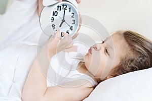 Dad wakes up little sleeping in bed girl,daughter. Big alarm,clock. Early morning before kindergaten, school. White pillow,