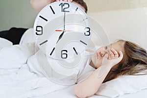 Dad wakes up little sleeping in bed girl,daughter. Big alarm clock. Early morning before kindergaten, school. White pillow,