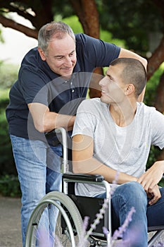 Dad walking with disabled son in wheelchair at park