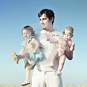 Daddy carrying children on his hands. Father and two daughters playing against blue sky