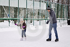 Daddy and daughter skate on the rink under the open sky on a winter day