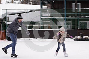 Daddy and daughter skate on the rink under the open sky on a winter day