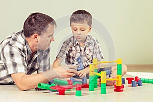 Daddy with little boy playing with toy on the floor at the day