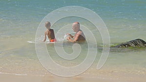 Daddy and little son swim in azure ocean on sunny day