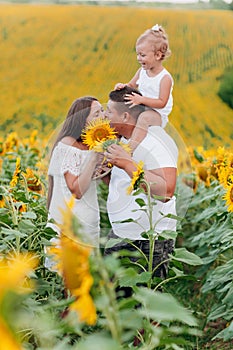 Daddy`s carrying a baby daughter on his shoulders in the field of sunflowers. The concept of summer holiday. Father`s