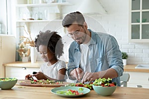 Daddy teach little African daughter cut vegetables prepare vegetarian salad