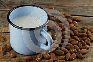 Dairy free almond milk in a blue cup and nuts on wooden background