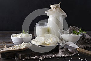 Dairy products on a dark background, a glass and a bottle of cow`s milk, cottage cheese, cheese, sour cream, white  eggs,  knife