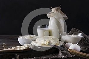 Dairy products on a dark background, a glass and a bottle of milk, cottage cheese, cheese, sour cream, eggs