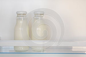 Dairy products in glass bottles on shelf of open empty fridge. White milk in refrigerator. Horizontal view with copy space