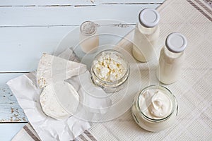 Dairy products. Milk in glass bottle, yogurt, sour milk cheese, sour cream in glass jar, camembert, brie on light wooden table