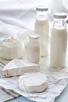 Dairy products. Milk in glass bottle, yogurt, sour milk cheese, sour cream in glass jar, camembert, brie on light wooden table