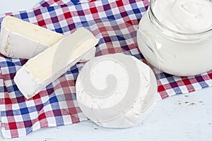 Dairy products. Sour milk cheese, sour cream, camembert and brie with checkered napkin on light blue wooden table