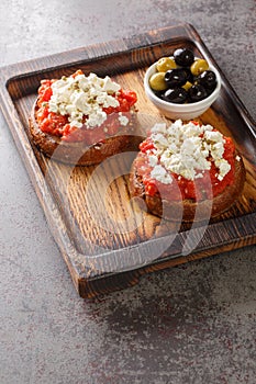 Dakos Cretan Meze appetizer with barley rusk, tomatoes, feta cheese, oregano and olive oil closeup on the wooden board. Vertical