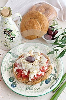 Dakos traditional Greek appetizer on a traditional plate with ceramic olive oil jar, dry rye bread, olives and olive branch.