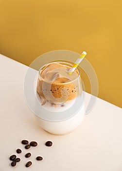 Dalgona coffee with milk in a glass with ice cubes and grains on a yellow background. The concept of a cold summer drink. Top view