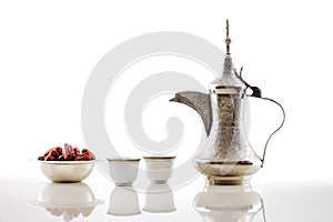 A dallah, a metal pot for making Arabic coffee with a bowl of dried dates photo