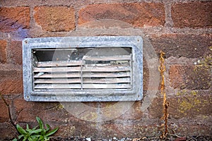 damaged air vent grill in a dirty red brick wall