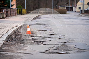 Damaged asphalt pavement road with potholes and traffic cone