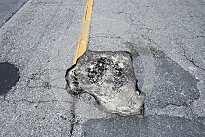 Damaged asphalt road with deep pothole on american highway surface. Ruined roadway in urgent need of repair