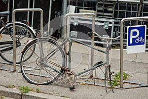 A damaged bike is locked in a bicycle stand.