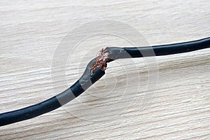 Damaged black electric cord on wooden floor background. Dangerous broken electrical cable