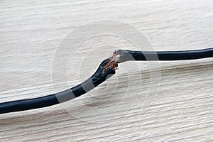 Damaged black electric cord on wooden floor background. Dangerous broken electrical cable