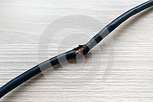 Damaged black electric cord on wooden table or floor background. Dangerous broken electrical cable