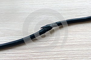 Damaged black electric cord on wooden table or floor background. Dangerous broken electrical cable