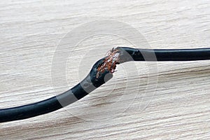 Damaged black electric cord on wooden table or floor background. Dangerous broken electrical cable photo