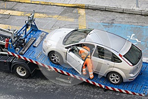 Damaged car being loaded onto tow truck by a worker