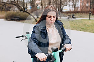 Damaged e-scooter for rent. Beautiful redhead 30s woman standing on modern scooter, frowning upset because of problem