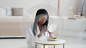 Damaged hair . Young unhappy african american woman in bathrobe looking at split ends of hairstyle, slow motion