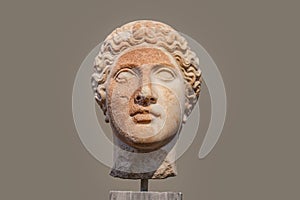 Damaged head of ancient Greek statue with part of face rough and orange from deterioration isolated against tan background