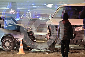 Damaged in heavy car accident vehicles after collision on city street crash site and silhouette of people at night. Road