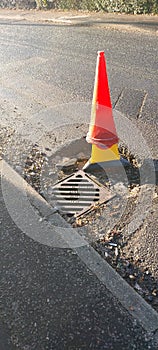 Damaged road with safety cone to warn drivers.